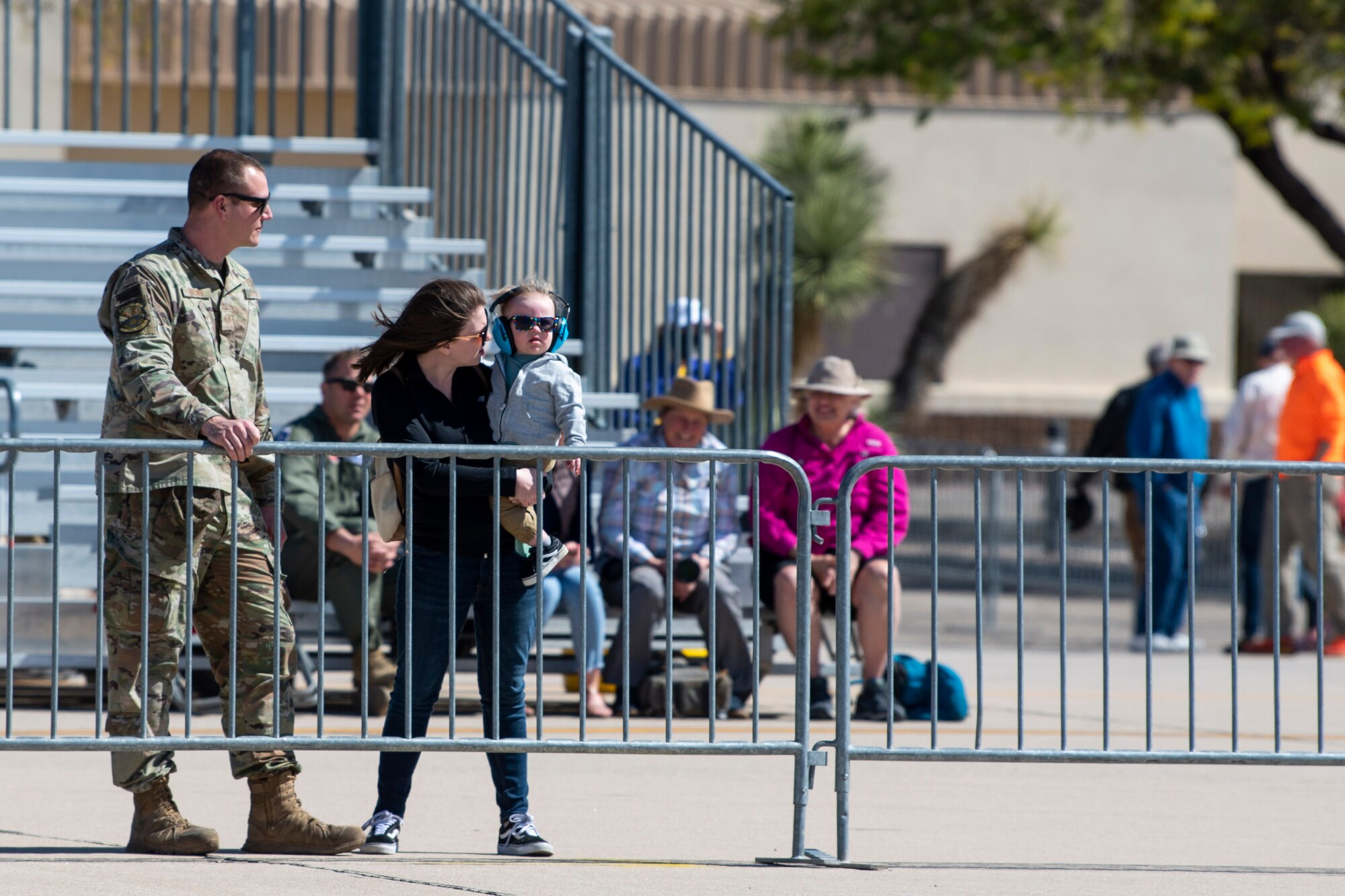 Crowd watches aircraft fly from behind a fence.