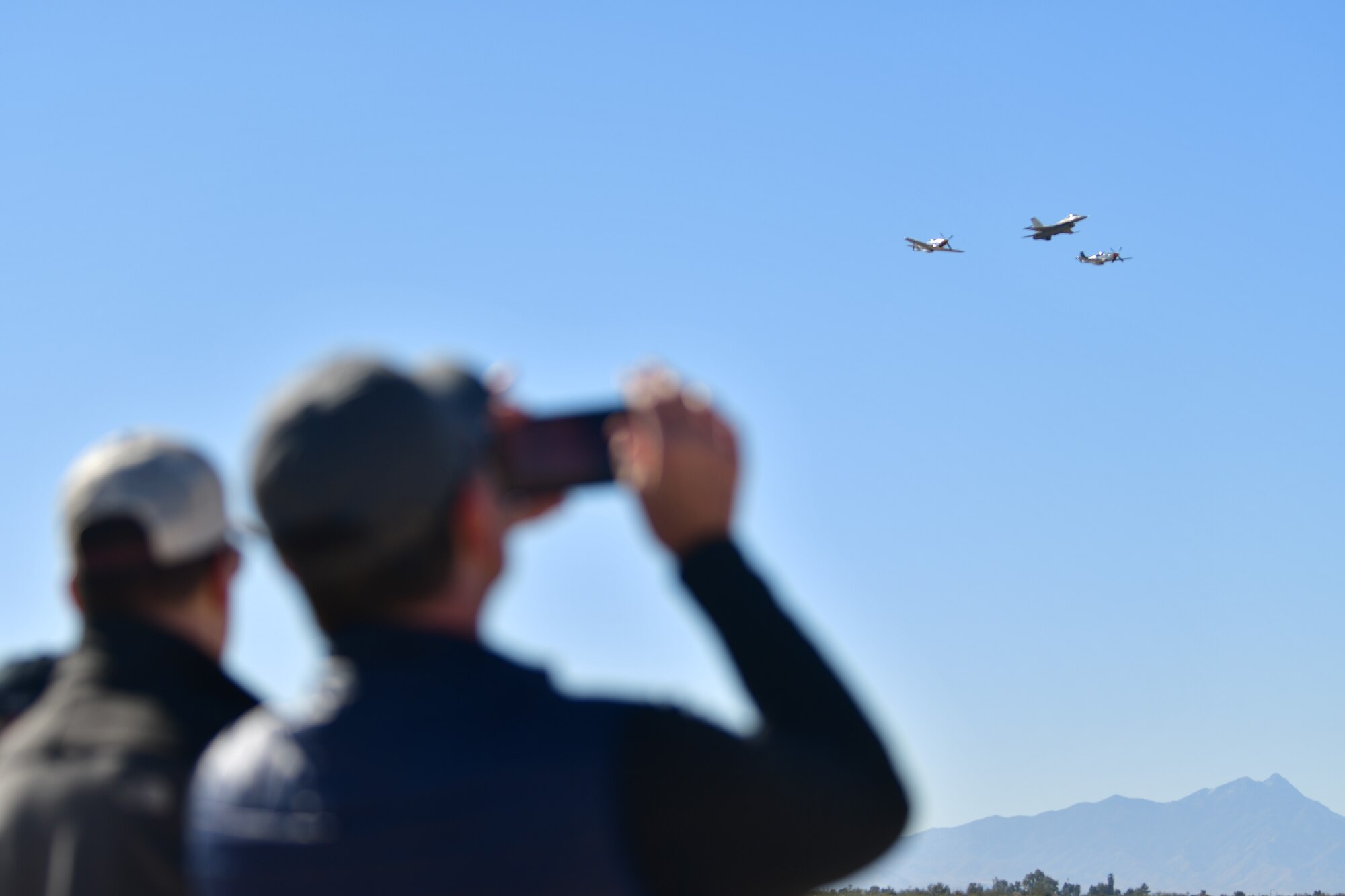 Two people watch three planes fly together in the distance.