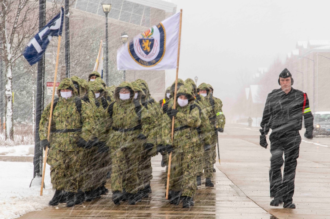 Navy recruits march in formation as snow falls.