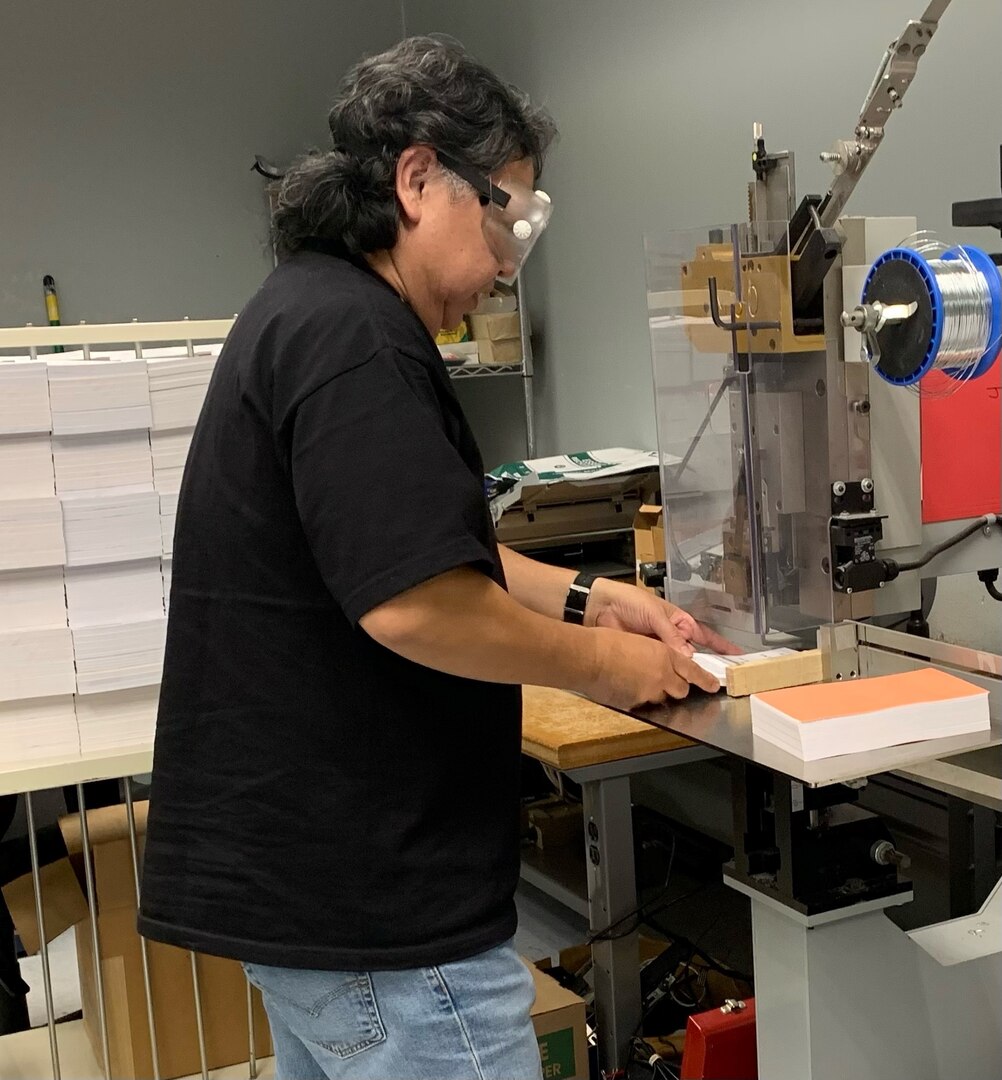 Male employee in a black shirt and safety glasses puts together the pages of a book.