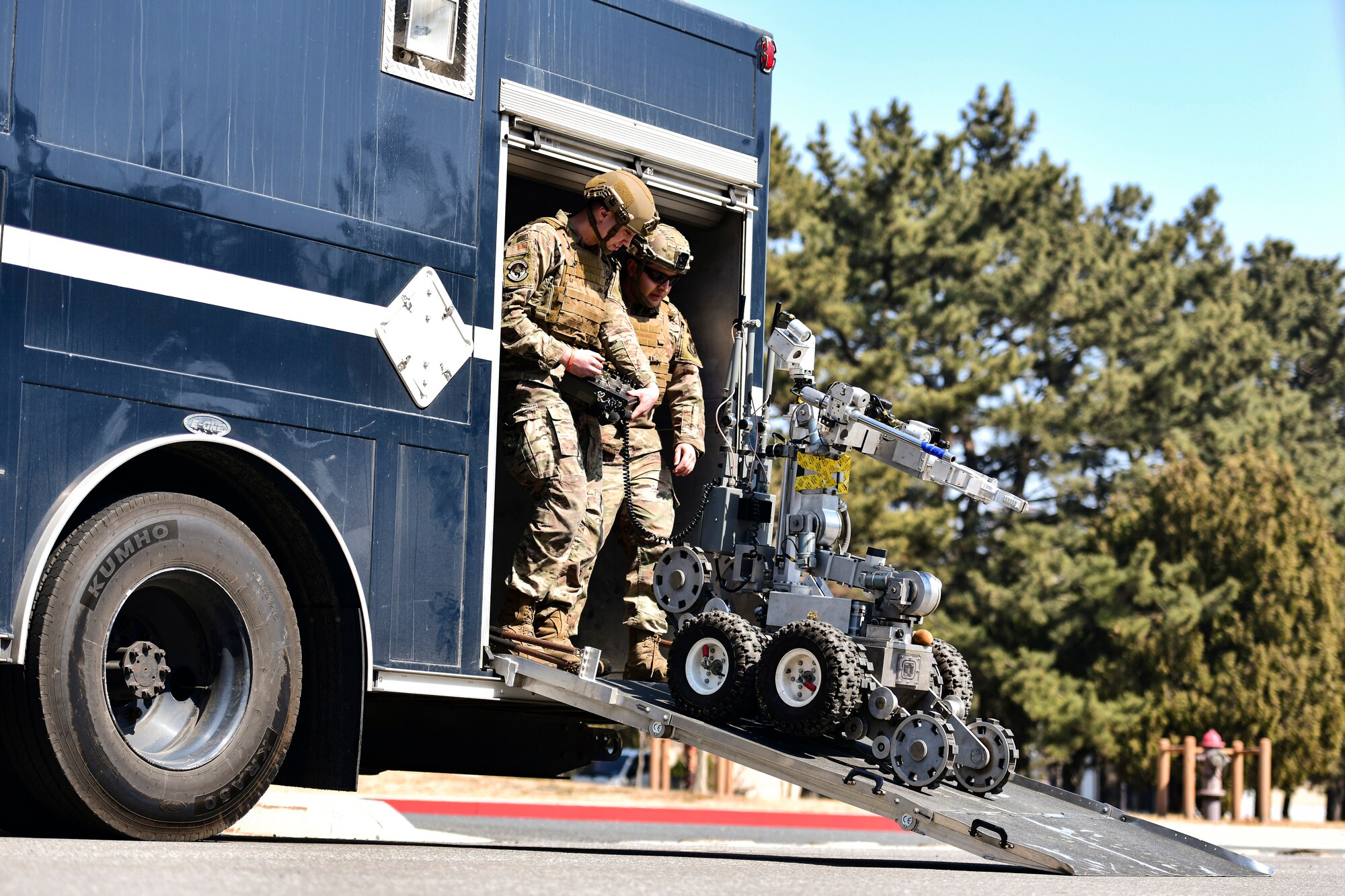 Airmen walk behind a robot.