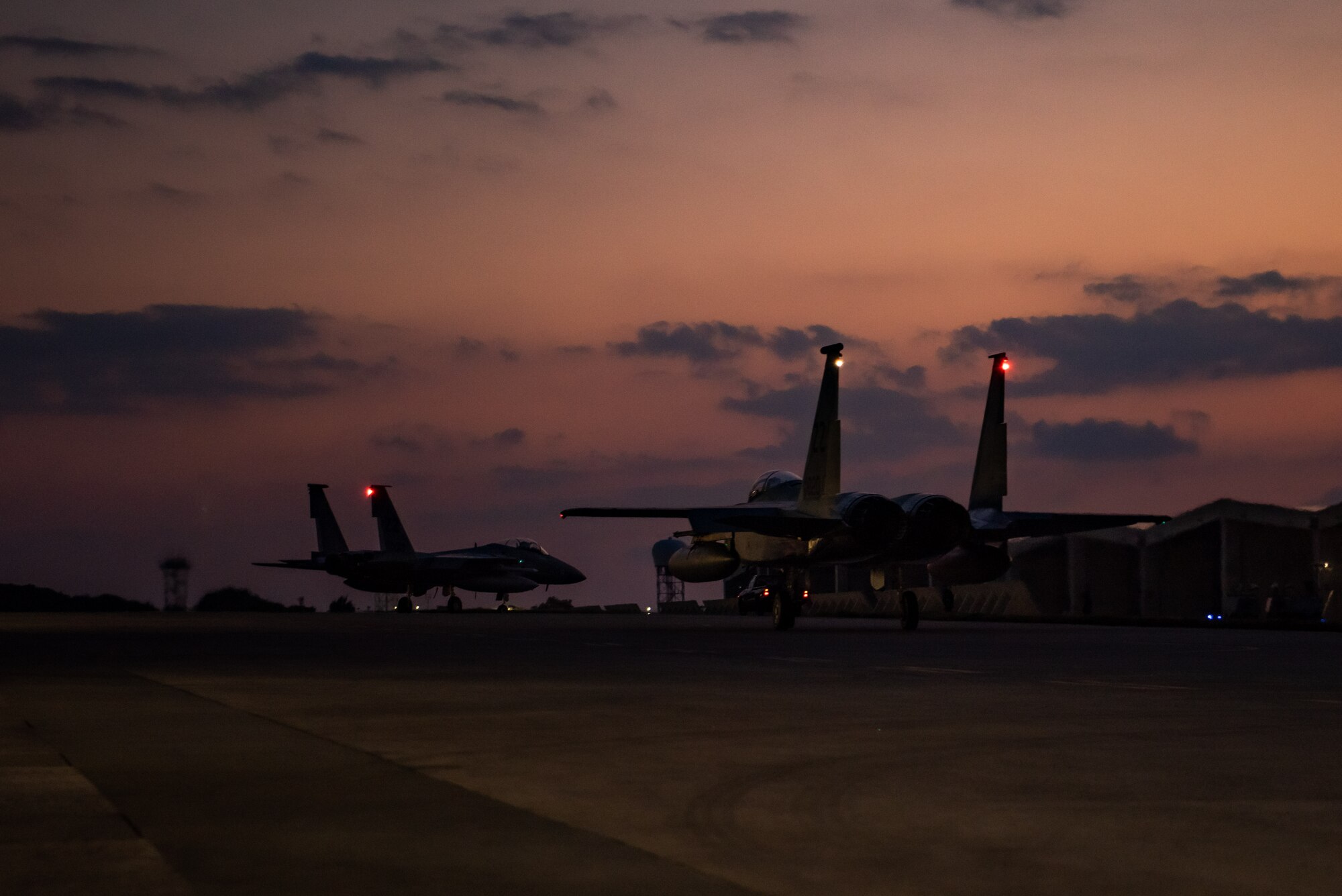 F-15C Eagles taxi on a flightline before takeoff at sunset.