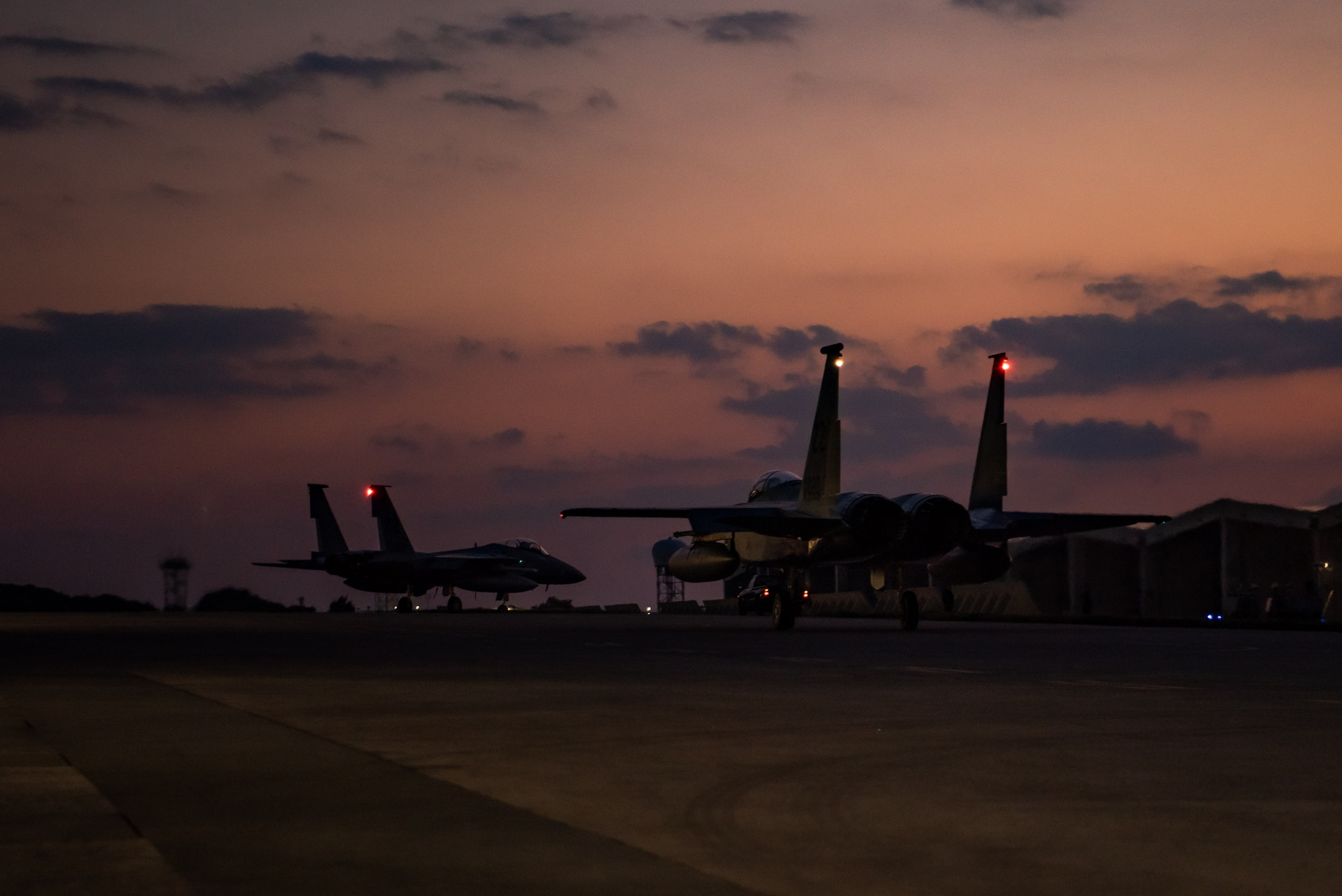 F-15C Eagles taxi on a flightline before takeoff at sunset.