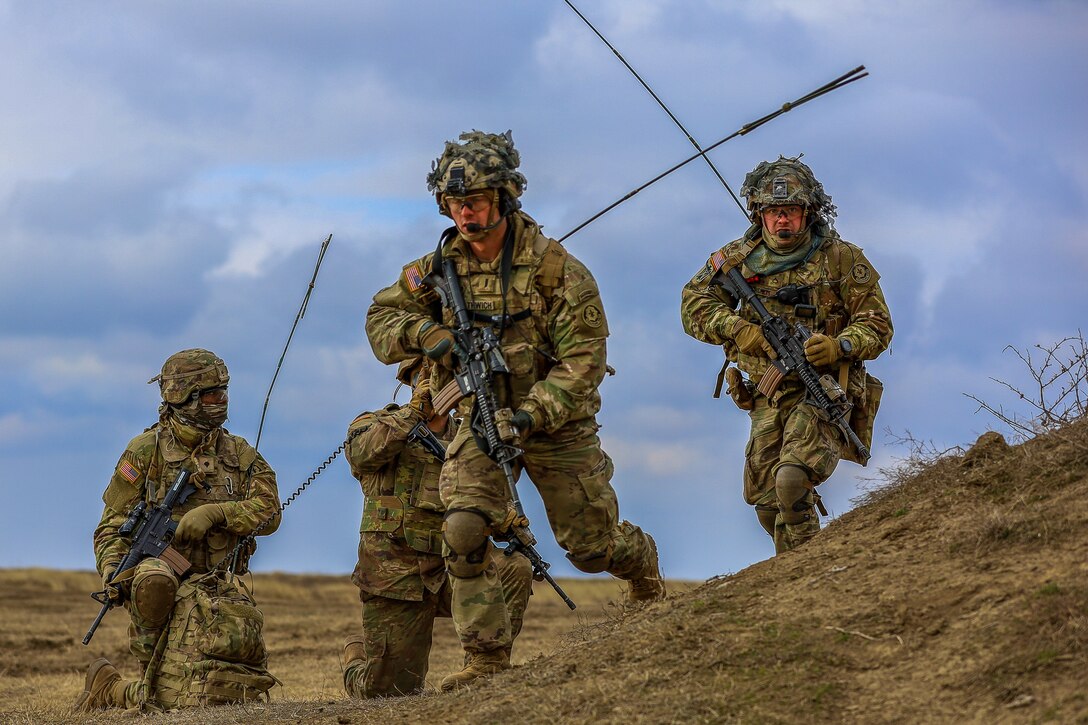 Four soldiers walk over a hilly field.