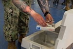 A servicemember's lower half is depicted as they unpack a package of pre-filled syringes of influenza vaccine.