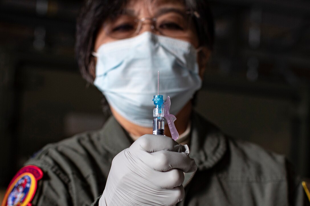 A woman in an Air Force flight suit holds a syringe containing the influenza vaccine.