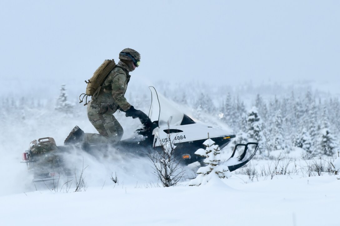 A soldier rides a snowmobile through the snow.