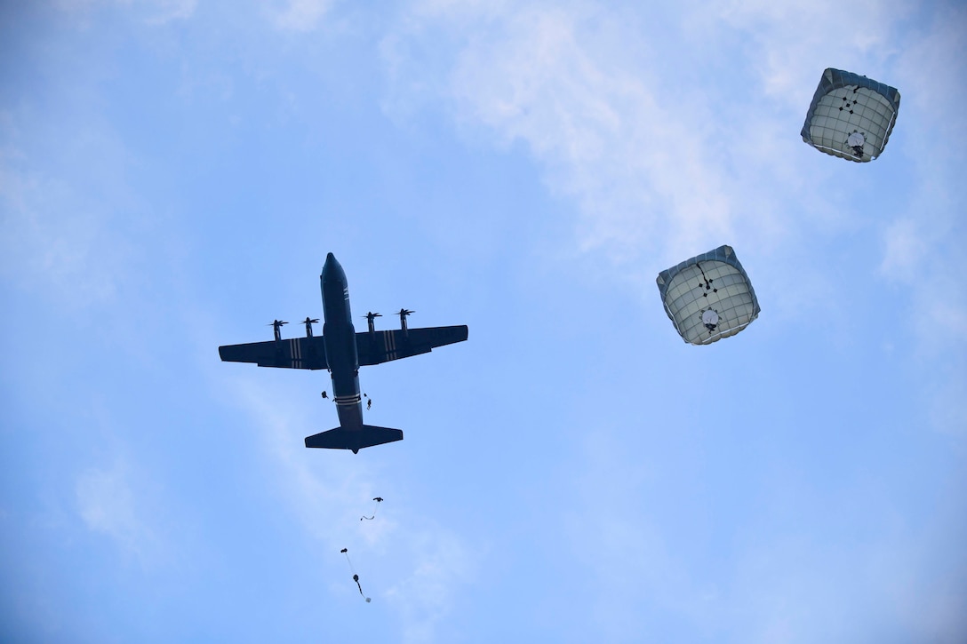 Soldiers jump from an airborne aircraft while wearing parachutes.