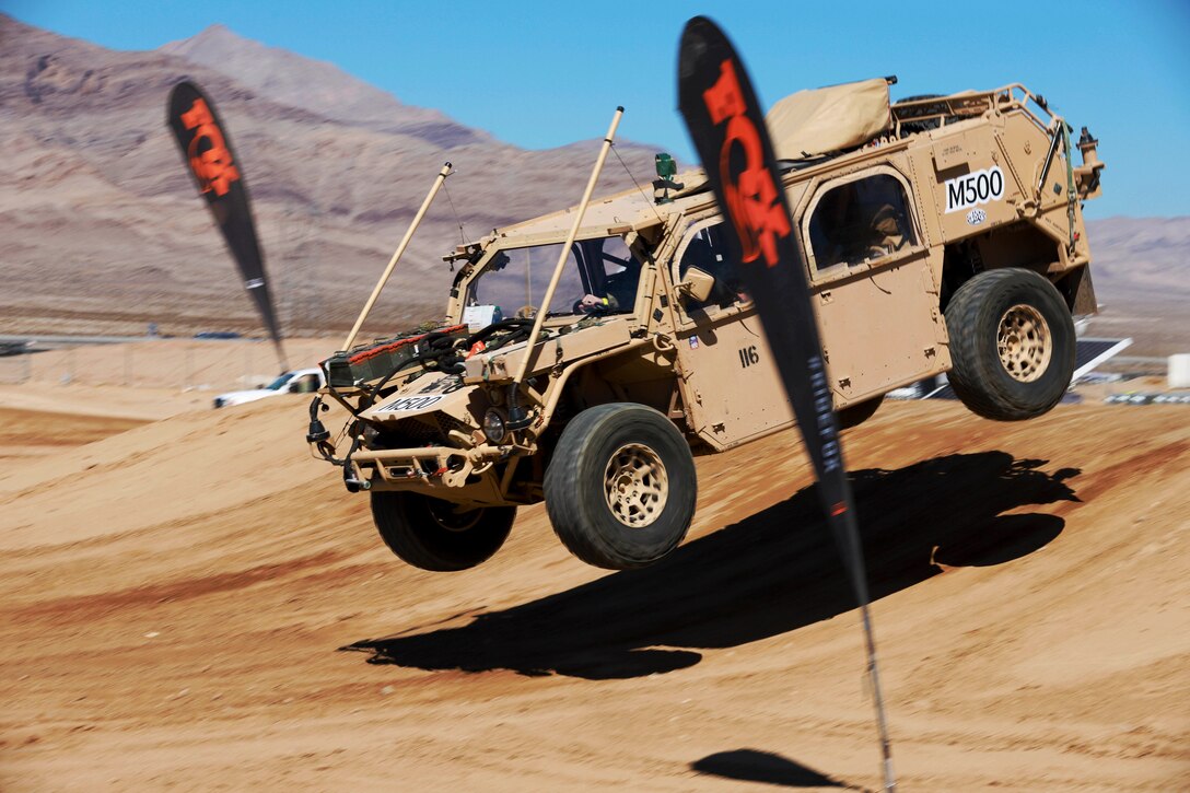 A large vehicle hits a jump during a race on a dirt road.