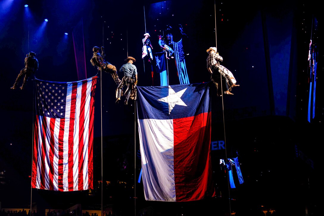 Airmen in cowboy uniforms hang from a ceiling along with a U.S. flag and a Texas flag.