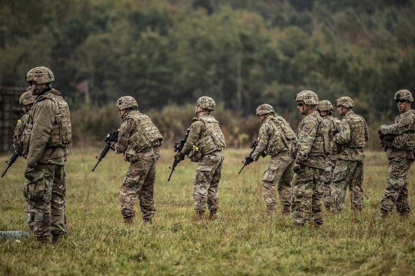 Uniformed personnel carry rifles outdoors.