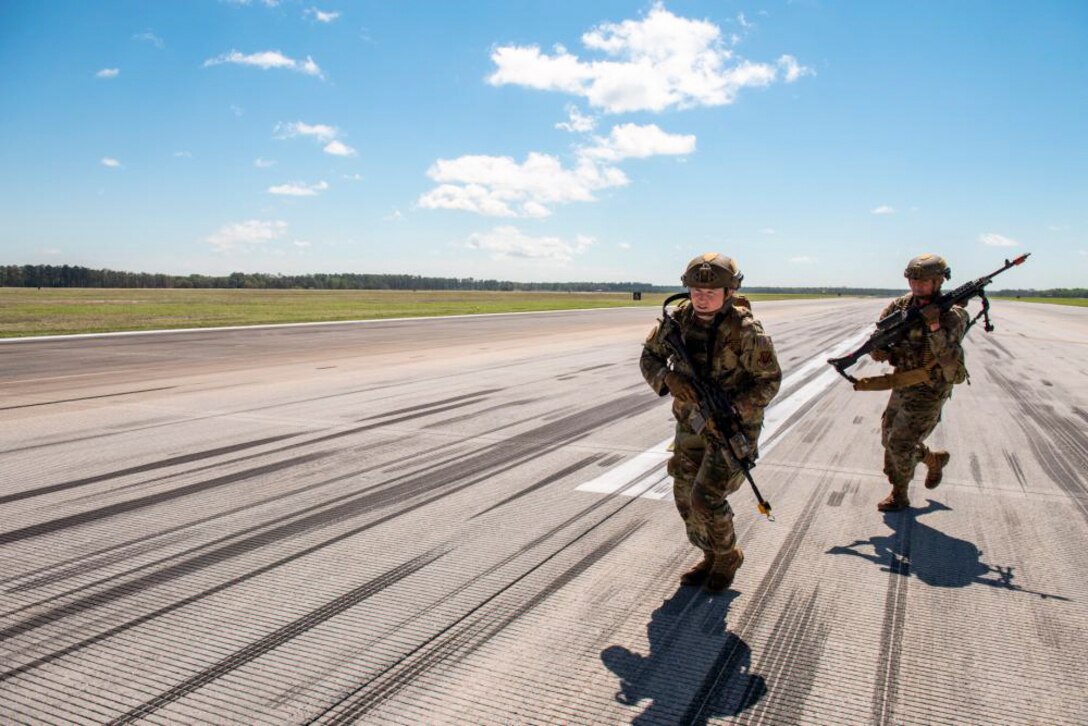 Two airmen holding weapons run on a tarmac during training.