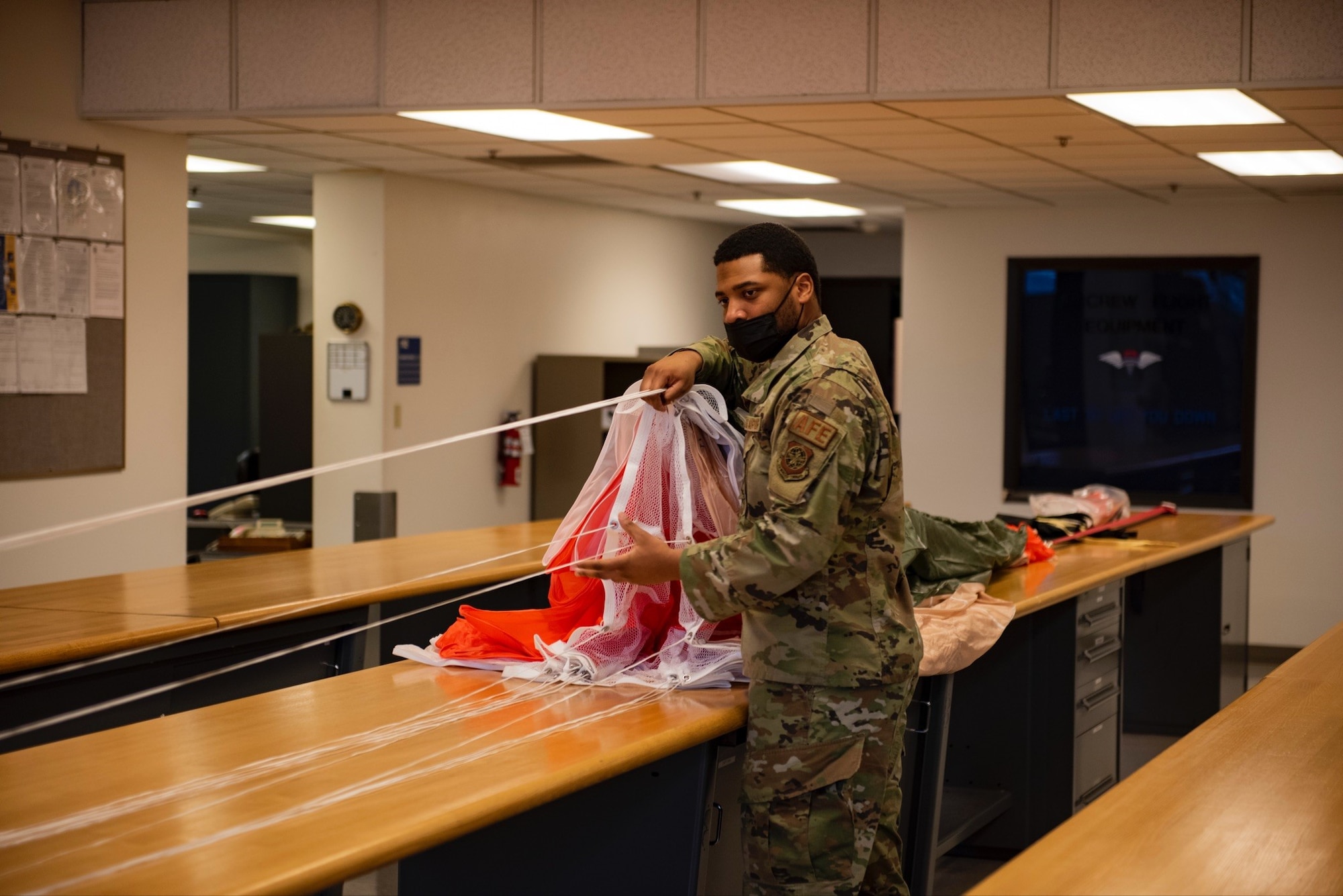 U.S. Air Force Staff Sgt. Glenn Marshall, 62nd Operations Support Squadron, NCO in charge of the parachute section, stretches a parachute along a worktable at Joint Base Lewis-McChord, Wash., Feb. 18, 2022. Proper installation, maintenance, and packing are necessary for the parachute to operate in as intended during a bailout situation. (U.S. Air Force photo by Tech. Sgt. Benjamin Sutton)