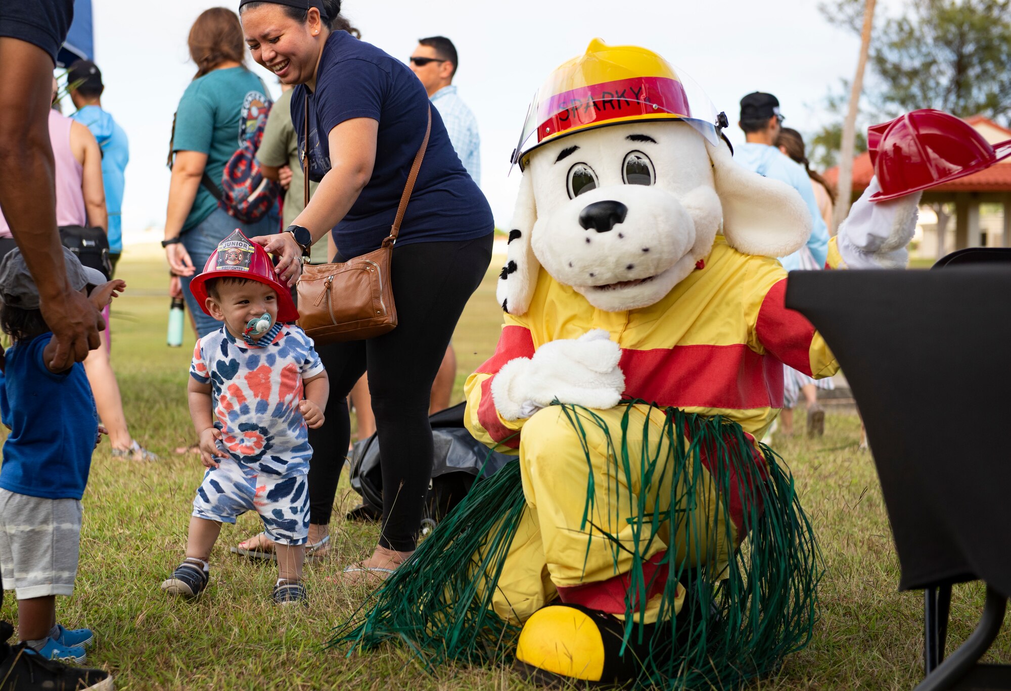 Sparky the dog hands out fireman hats to the children of Team Andersen during the annual Tao Tao Guahan event March 12, 2022, at Andersen Air Force Base, Guam. The event focused on immersing Team Andersen members in the local culture of Guam and strengthen the partnerships of the two communities. The event included booths, cultural music and dance, storytelling, food and more. (U.S. Air Force Photo by Senior Airman Helena Owens)