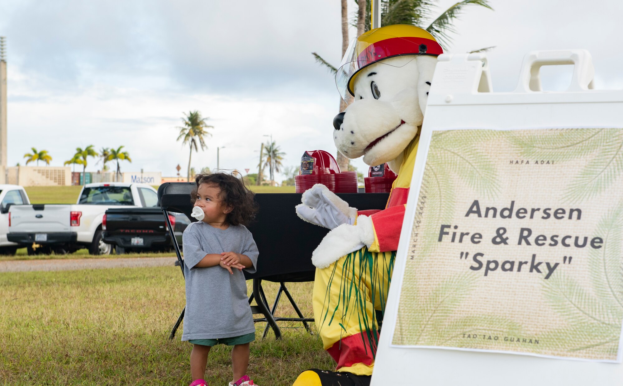 Sparky the dog poses for a photo with a Team Andersen child during the annual Tao Tao Guahan event March 12, 2022, at Andersen Air Force Base, Guam. The event focused on immersing Team Andersen members in the local culture of Guam and strengthen the partnerships of the two communities. The event included booths, cultural music and dance, storytelling, food and more. (U.S. Air Force Photo by Senior Airman Helena Owens)