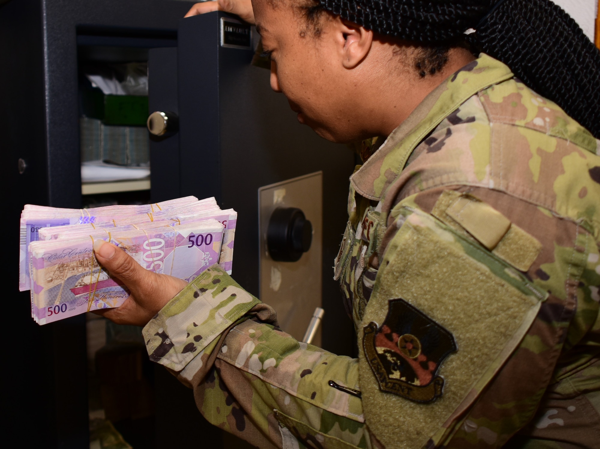 photo of a female military Airman storing Qatari Riyal into a  medium-sized office safe