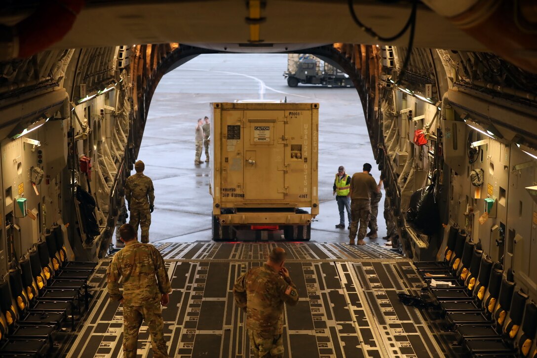 Airmen guide a medium tactical vehicle onto a C-17 Globemaster..
