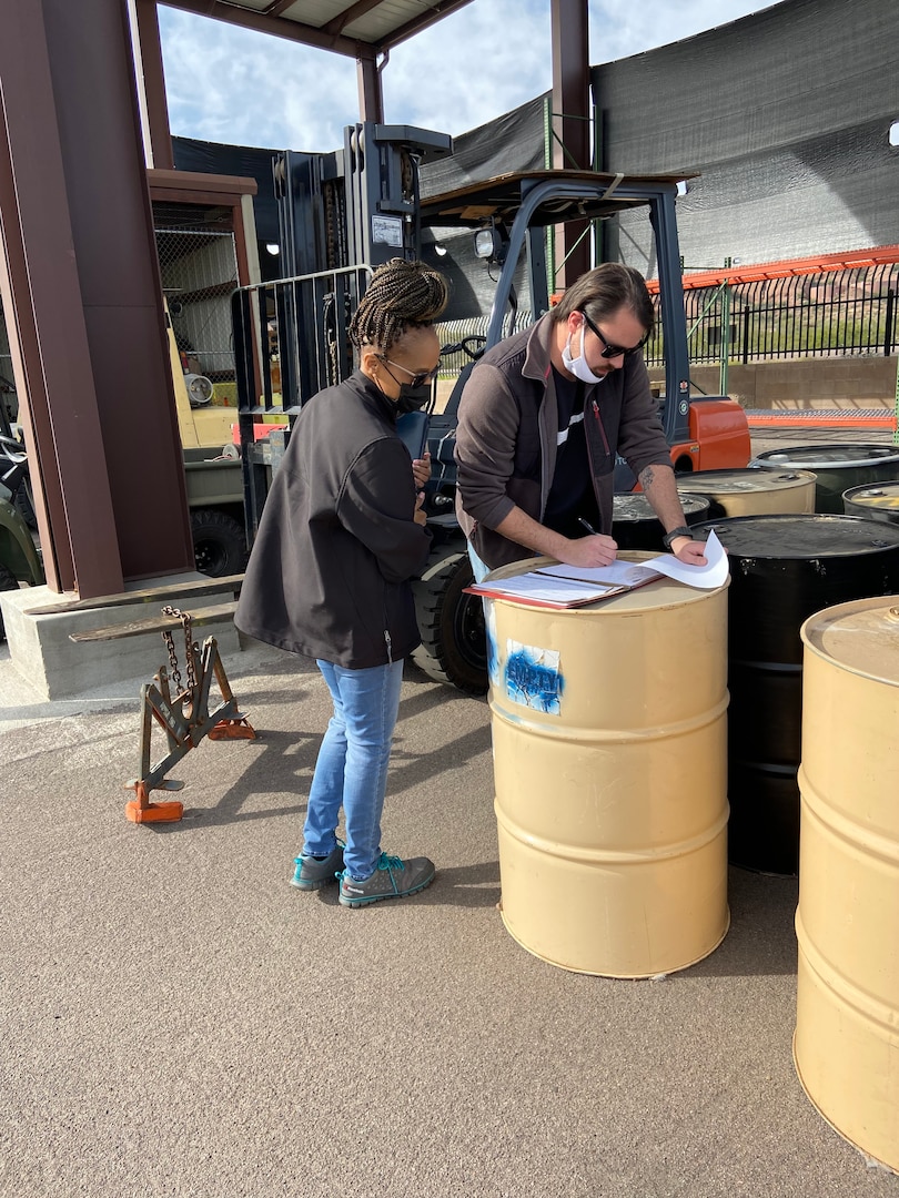 Two men look at paperwork on top of a barrel