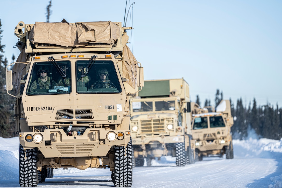 Large military trucks drive along a snowy road.