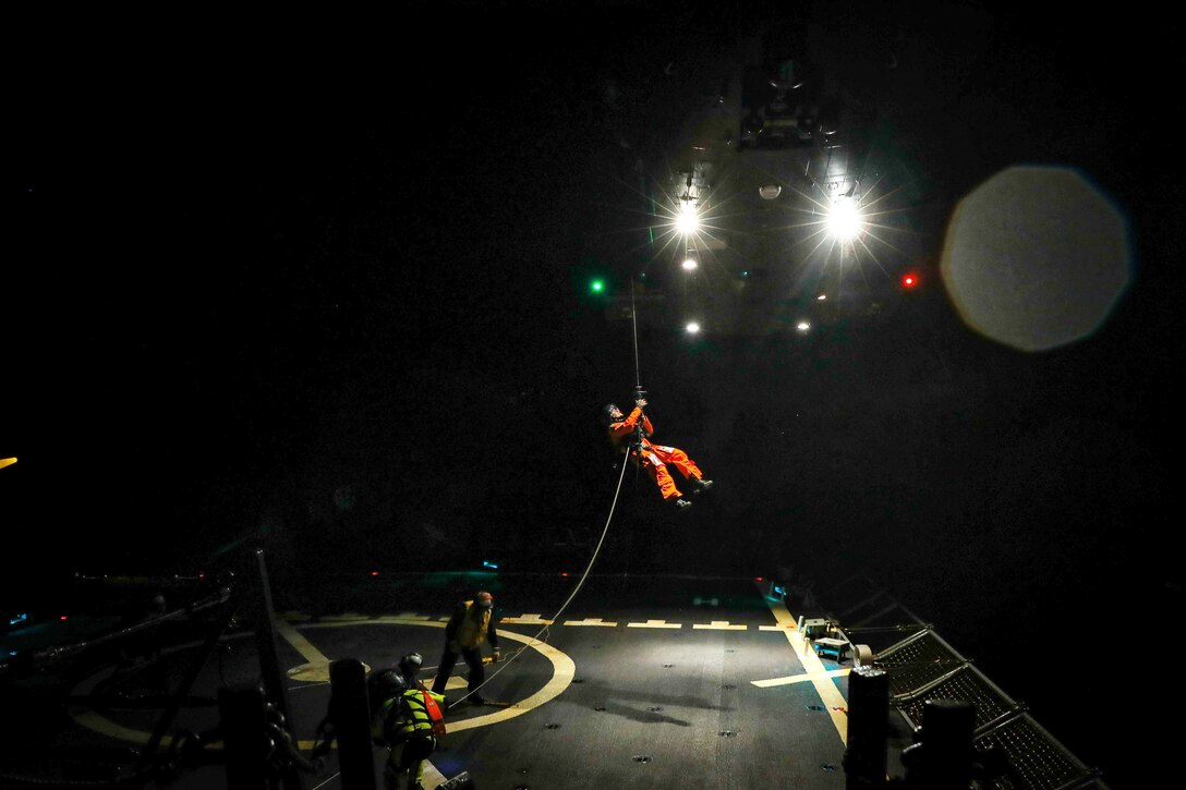 A sailor holds onto a winch at night.