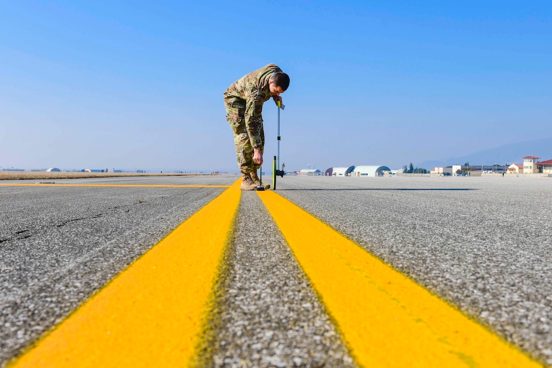 An airman uses a tool on yellow lines on the ground.