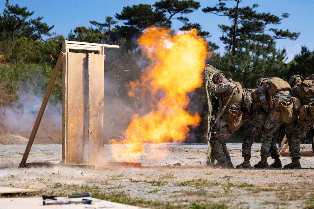 Marines stand huddled together in a line as an explosive detonates.