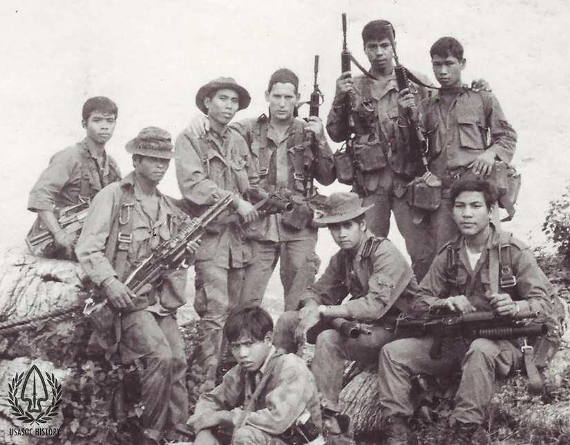 Nine men in combat uniform, all of whom carry large rifles, pose for a photo.