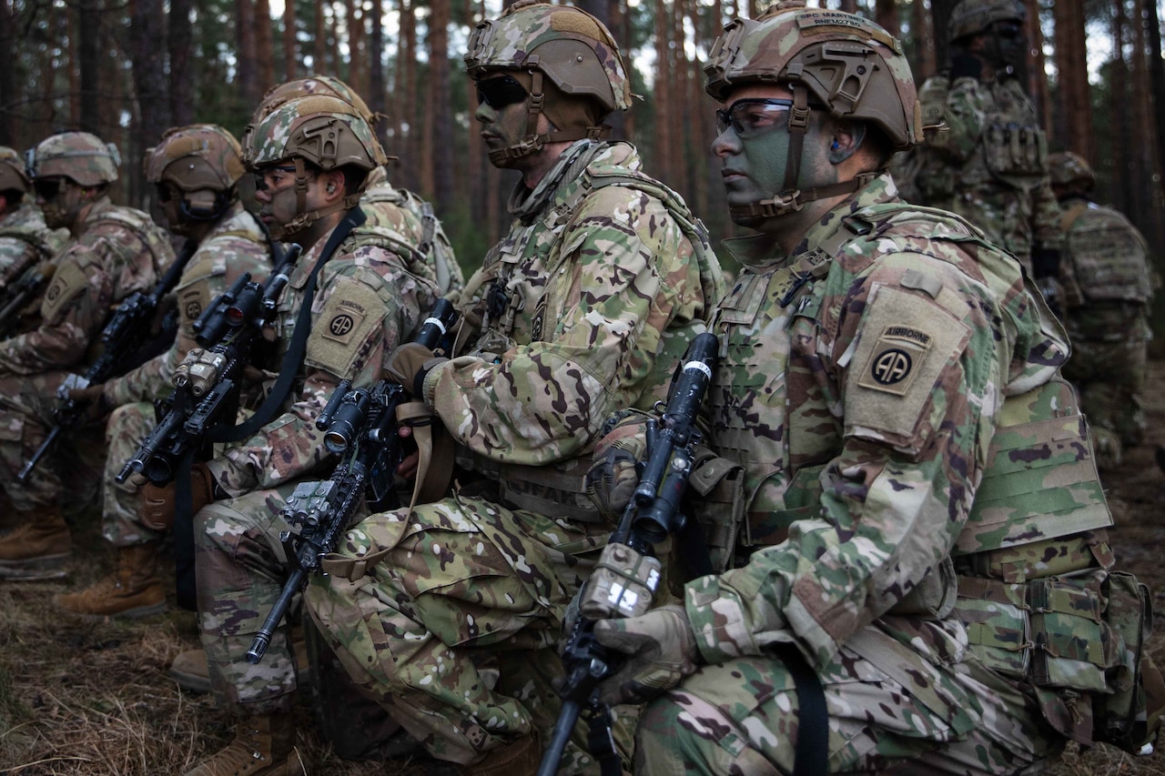 Troops in camouflage wait for a transport helicopter.