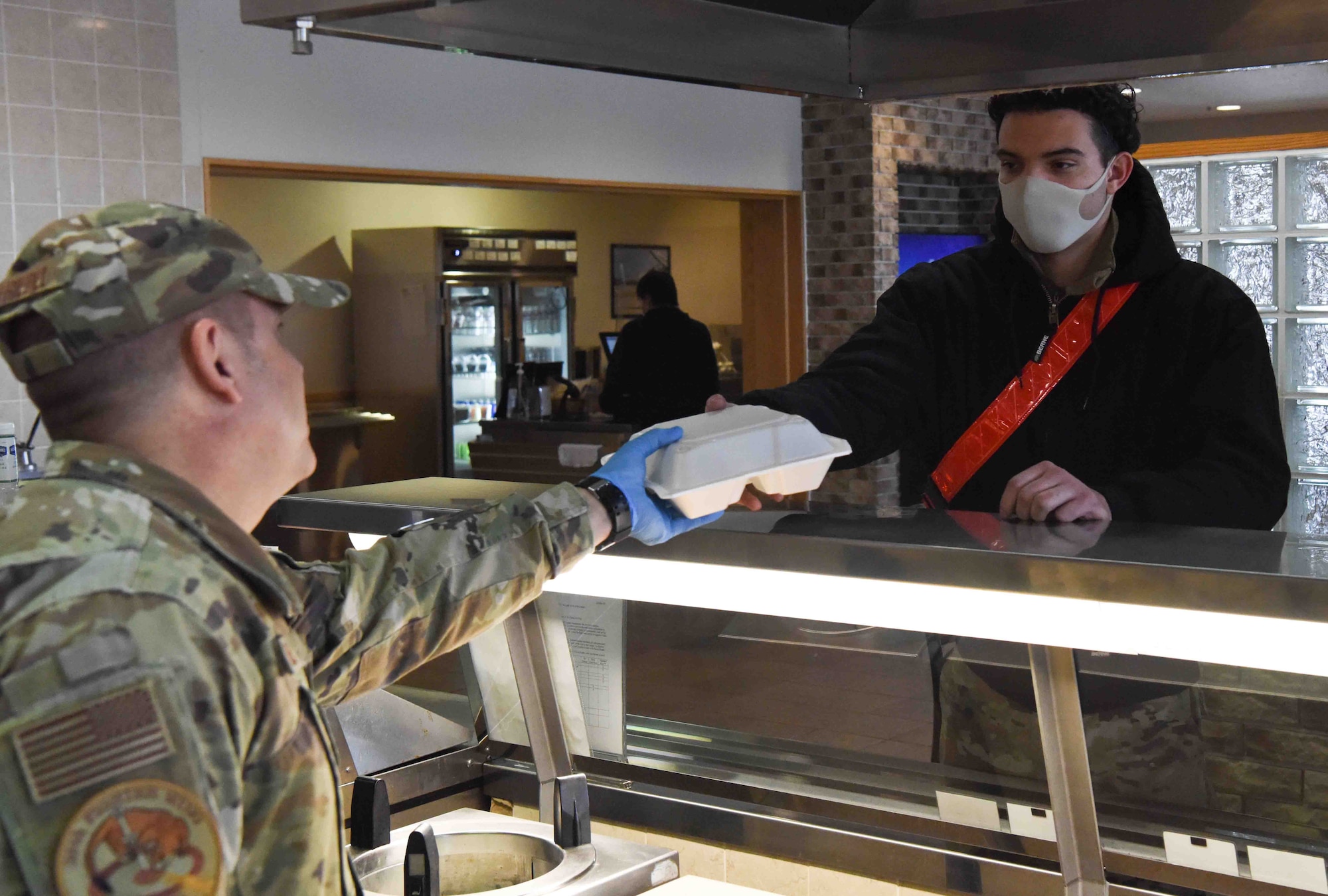 A service member hands a plate of food to another service member.