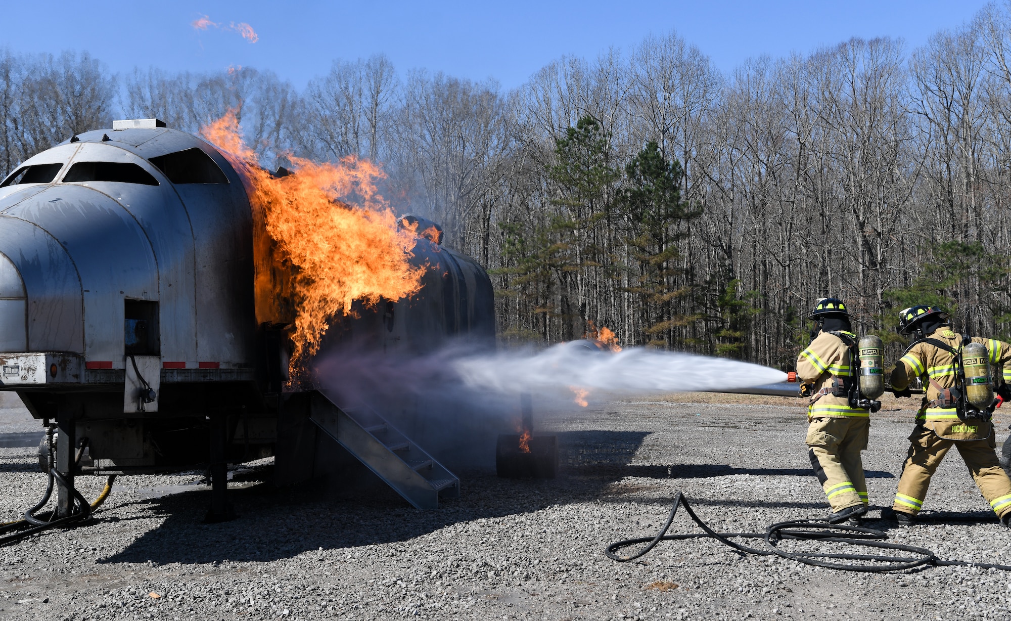 Chief Master Sgt. Jennifer Cirricione in firefighter gear operating hose backed up by Adam McKamey