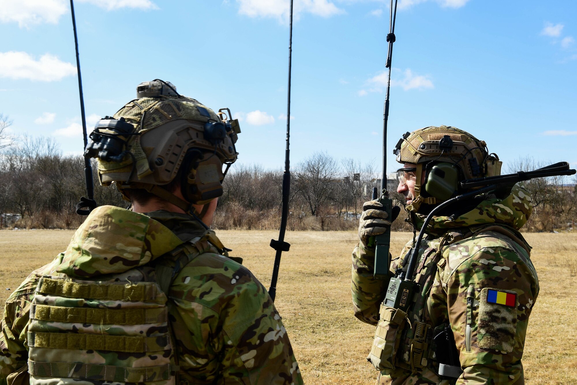 U.S. Air Force 1st Lt. Alexander Mount, 57th Rescue Squadron combat rescue officer, left, teaches how to call in a helicopter for extraction in Romania, March, 9, 2022. The 57th RQS and the 56th RQS alongside the Royal Marines Commando Mobile Air Operations team with Commando Helicopter Force provided training on how to safely operate around a helicopter to the 51st Commando Battalion Romanian Special Forces. (U.S. Air Force Photo by Senior Airman Noah Sudolcan)