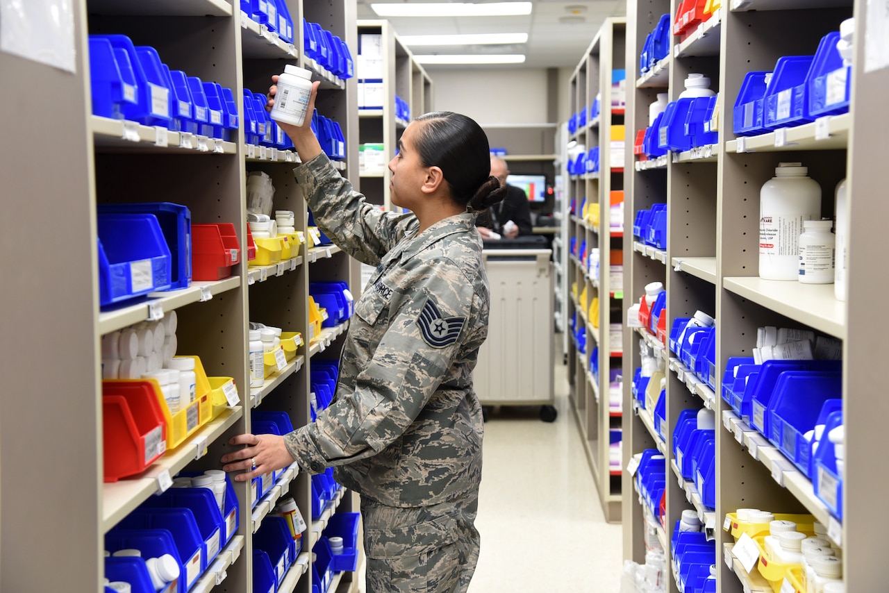 A female service member takes a plastic bottle from a bin on a shelf with many other bins.