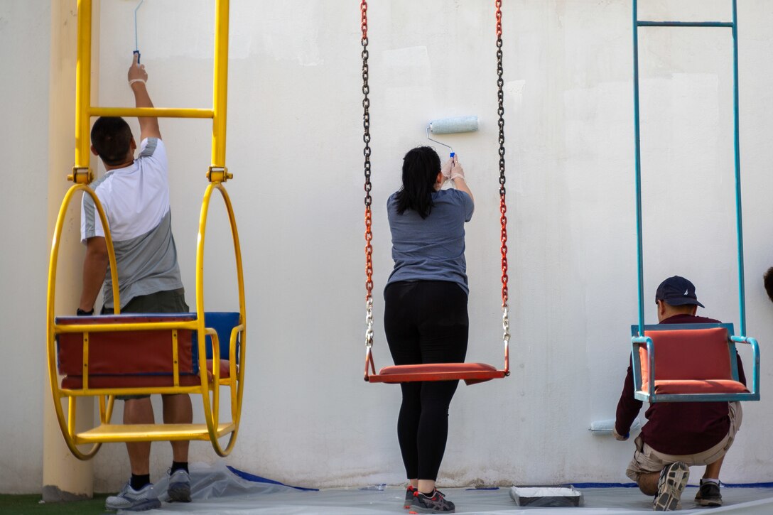 Three sailors paint a wall.