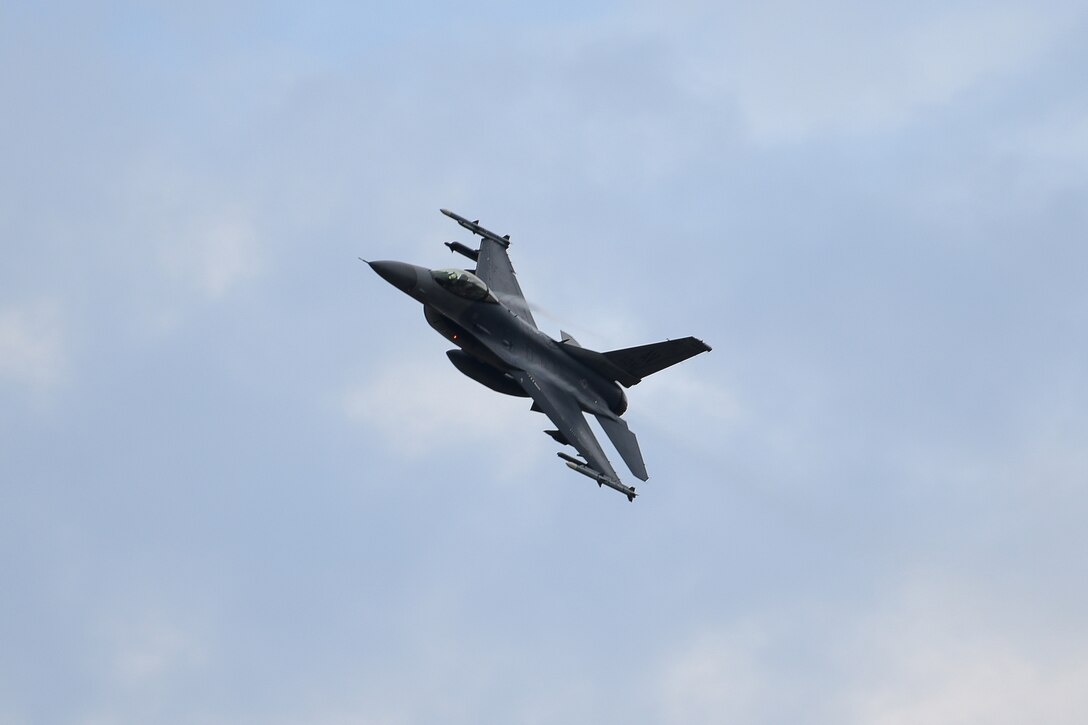 A military jet flies across a blue sky.