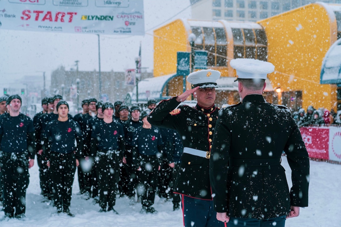 A Marine salutes another Marine during a ceremony in the snow.