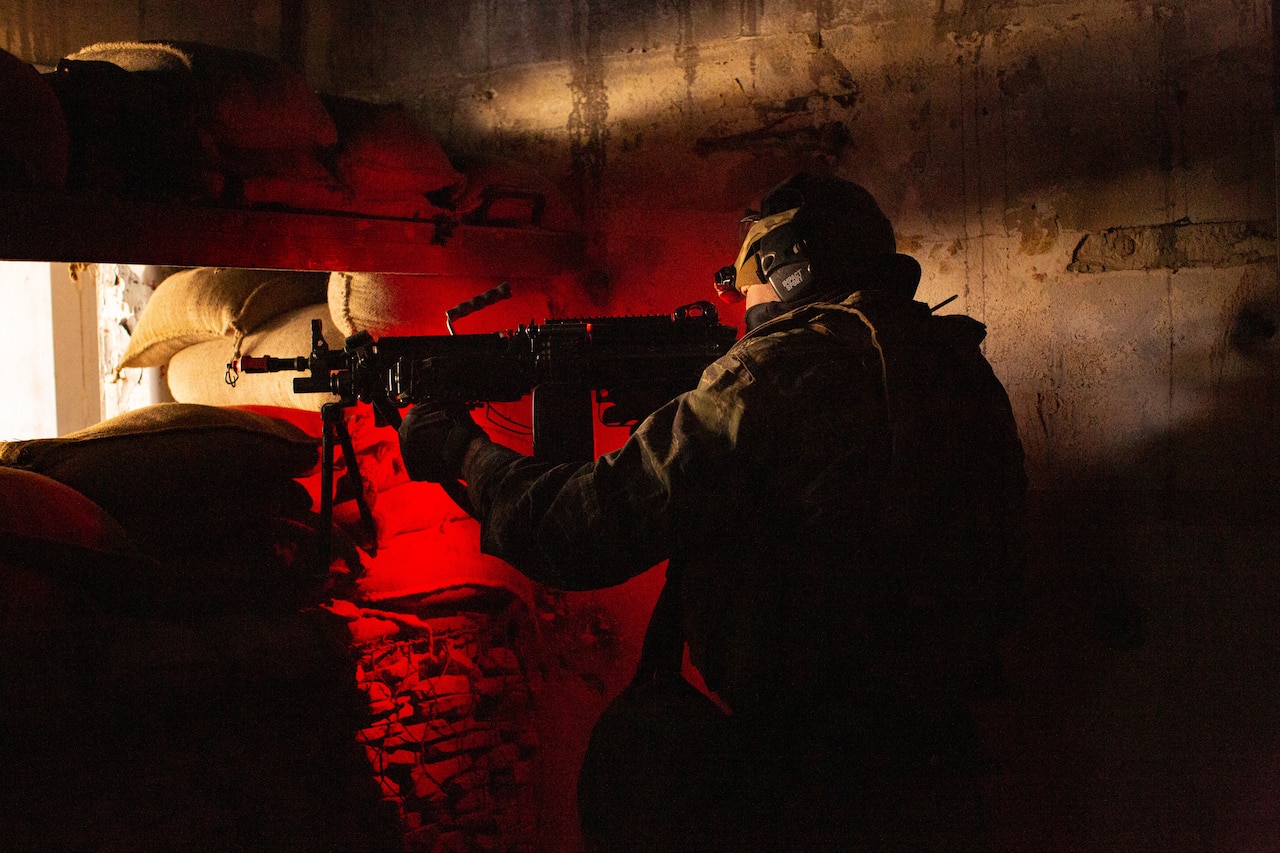 A service member inside a bunker aims his rifle.