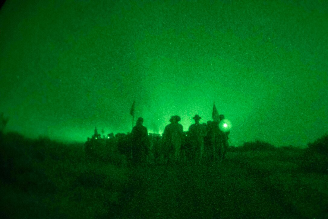 Marine Corps recruits illuminated by green light march at night.