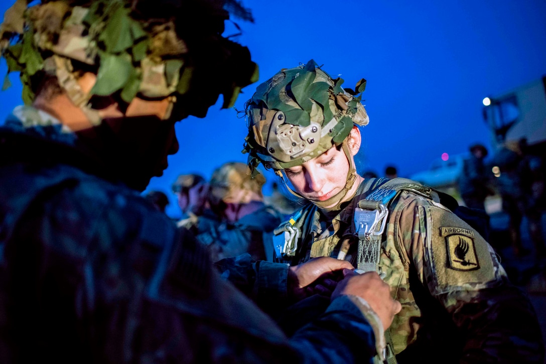 A soldier secures a parachute on another soldier.