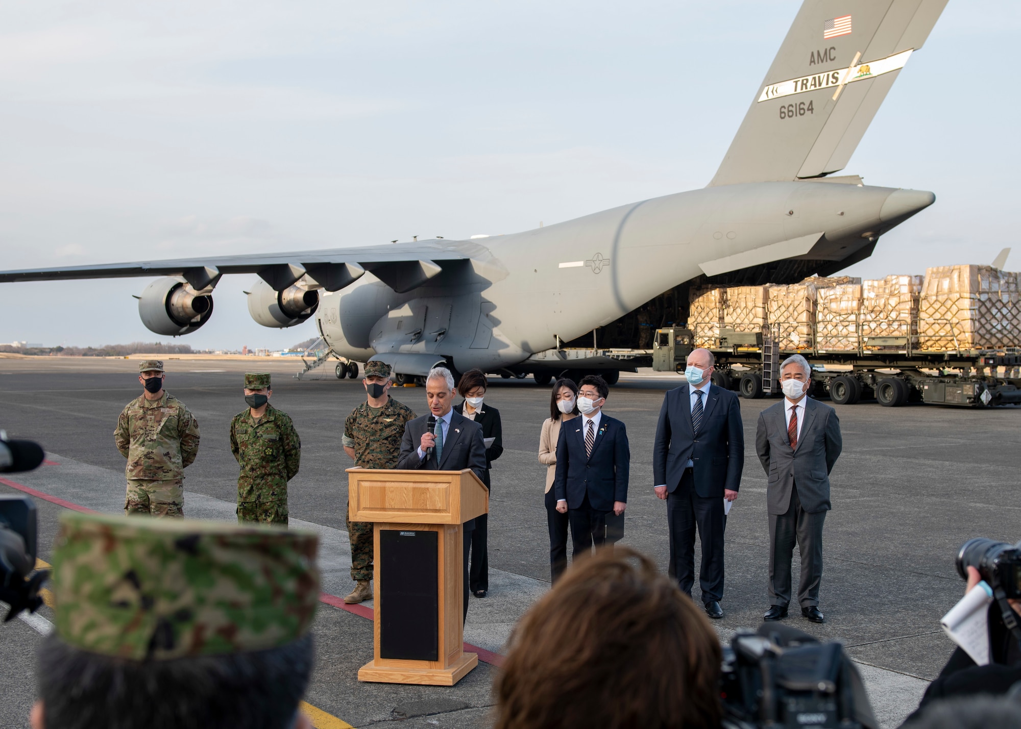A politician speaks to a crowd gathered in front of a military cargo aircraft.