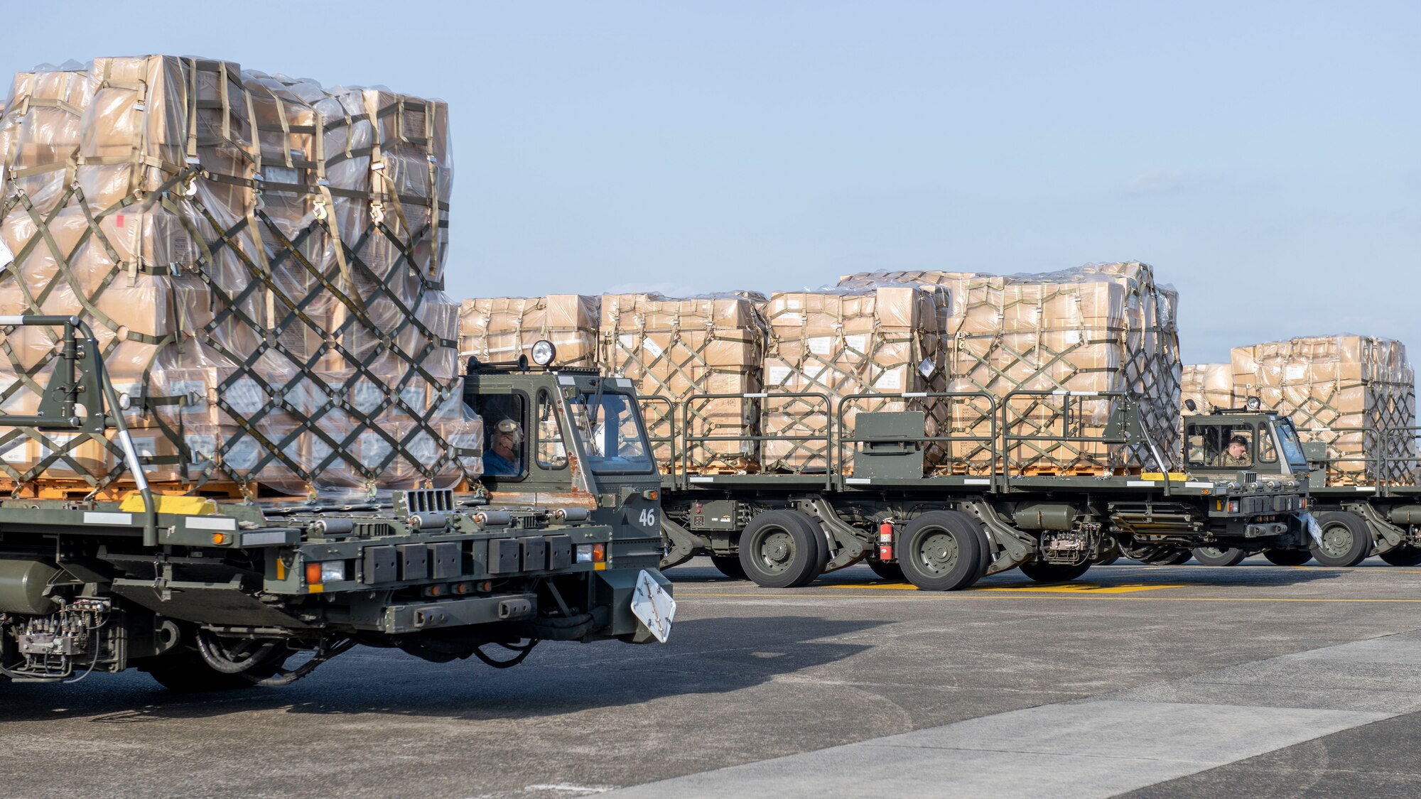 Three heavily loaded cargo trucks wait on a flight line.