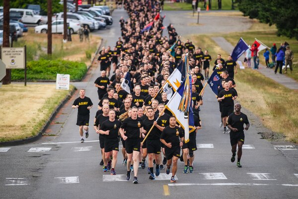 Large group of soldiers from I Corps wearing black PT uniform run on pavement with Command Sgt. Major Walter A. Tagalicud leading.