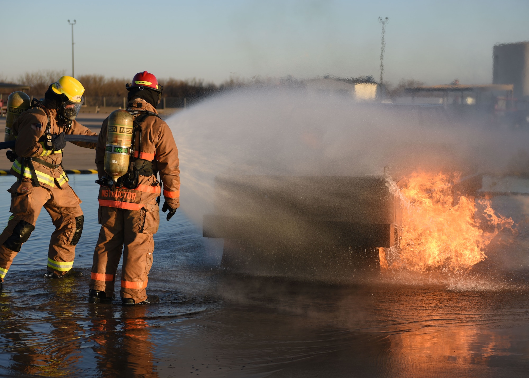 A Department of Defense instructor, right, assigned to the 312th Training Squadron 
coaches students through extinguishing a vehicle fire at the Louis F. Garland DoD Fire Academy, Goodfellow Air Force Base, March 9, 2022. Joint service students attend the apprentice course for 68 academic days, graduating with multiple certificates. (U.S. Air Force photo by Airman 1st Class Sarah Williams)