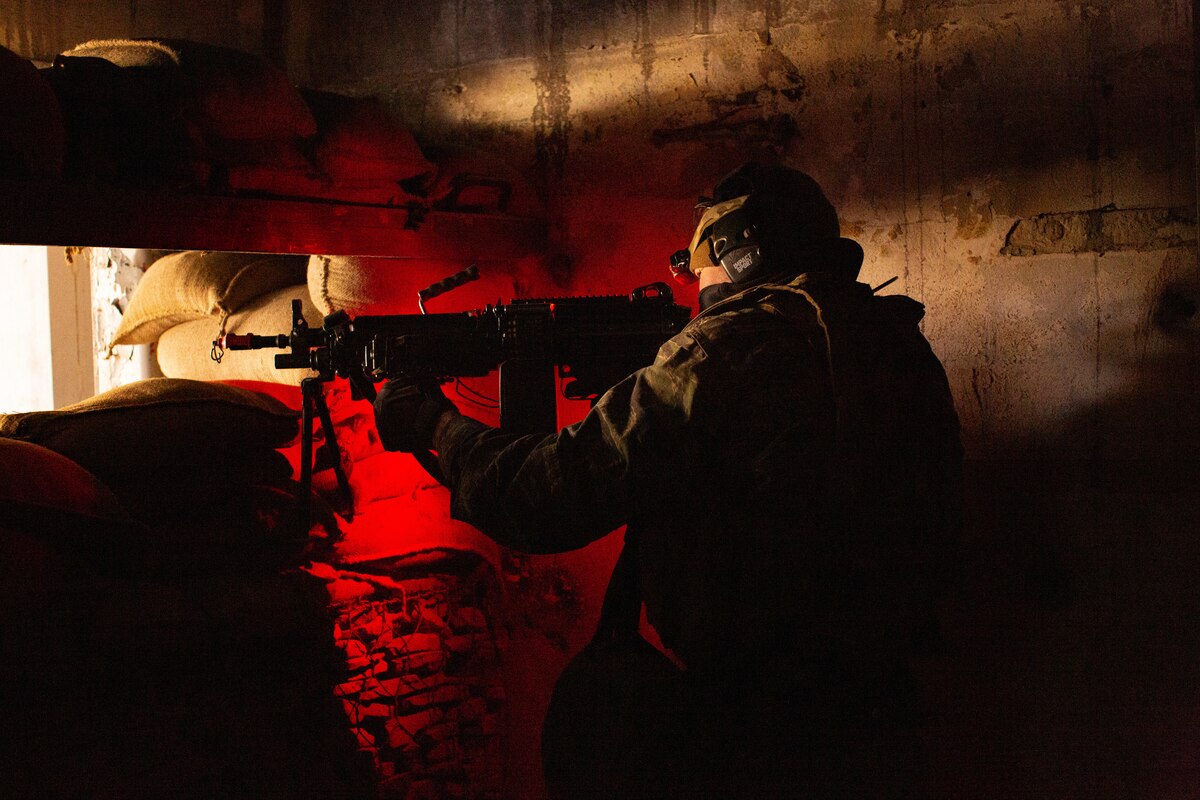 A service member inside a bunker aims his rifle.