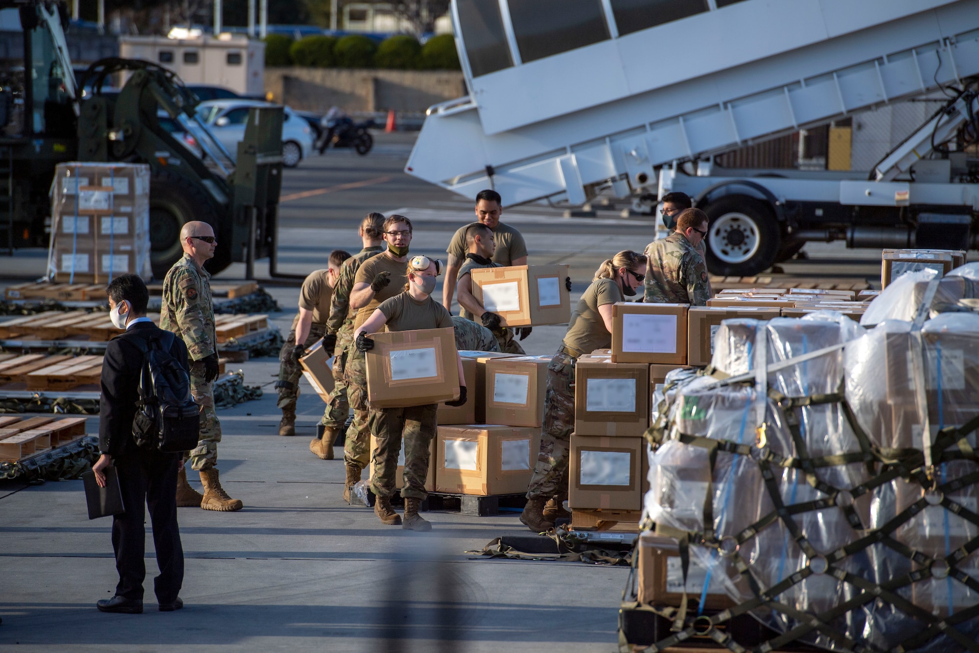 A dozen cargo Airmen load boxes onto a large pallet.
