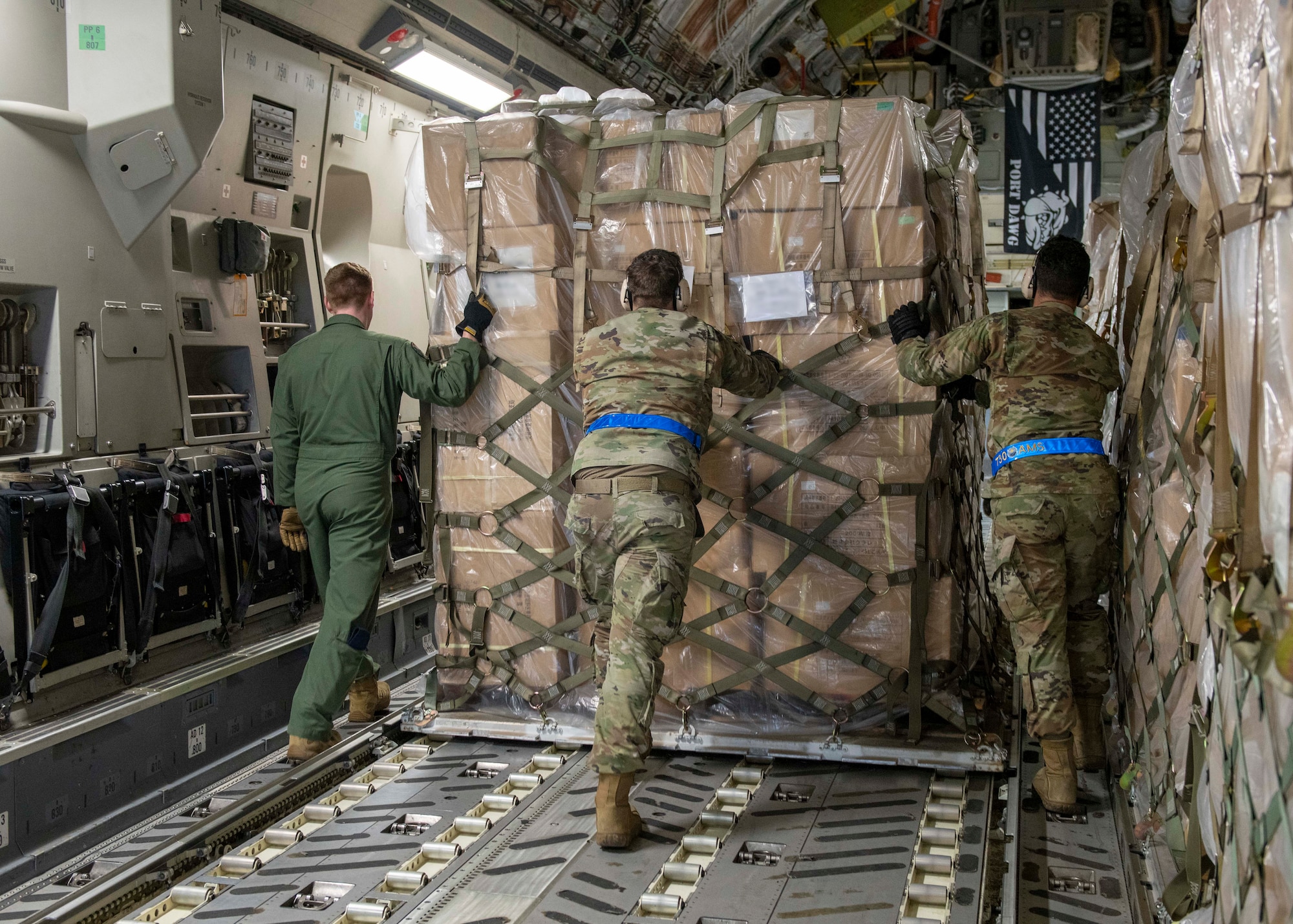 Three Airmen push a large pallet of boxes into the cargo hold of an airplane.