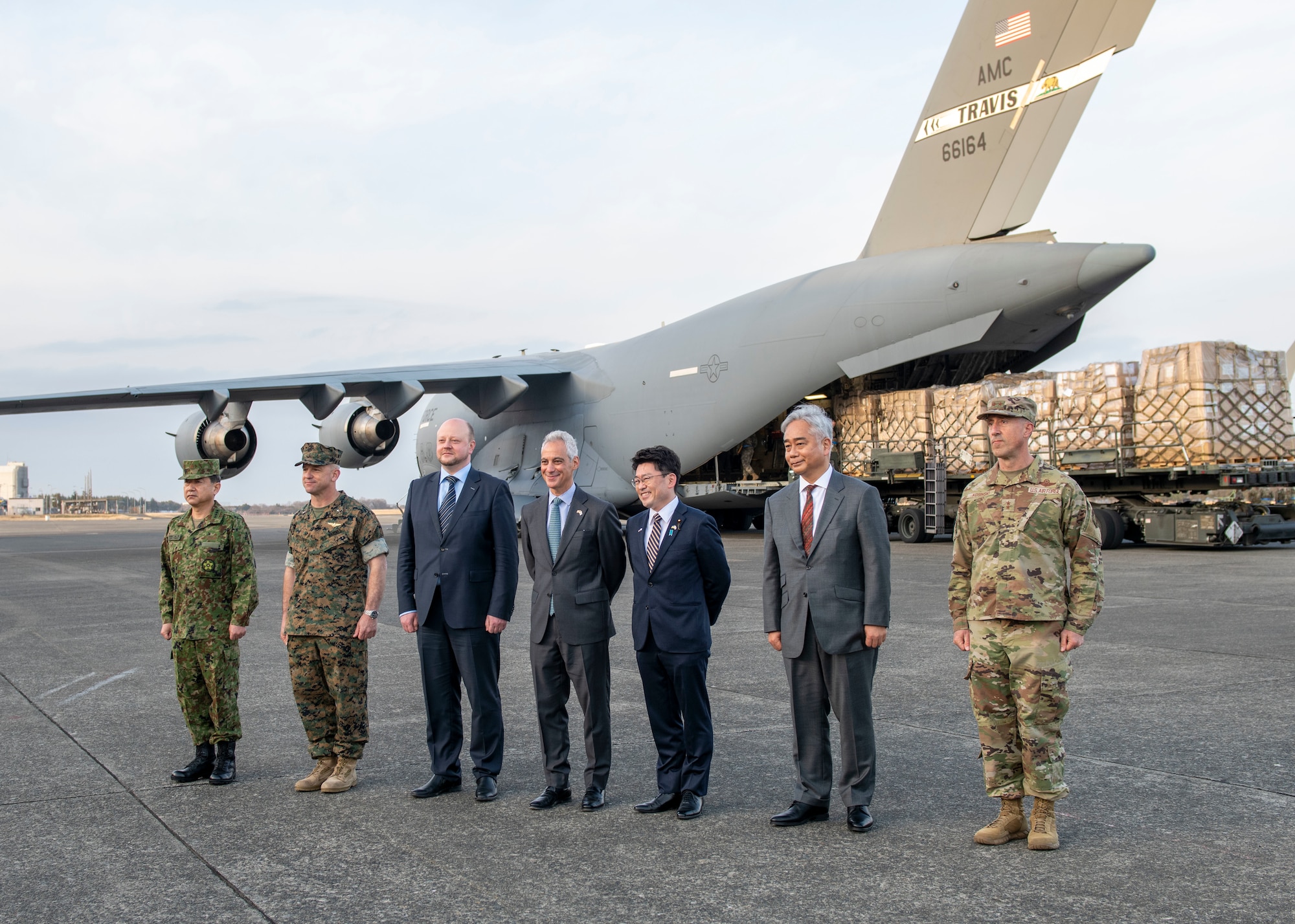 A line of government officials and military leaders stand in front of a military cargo aircraft.