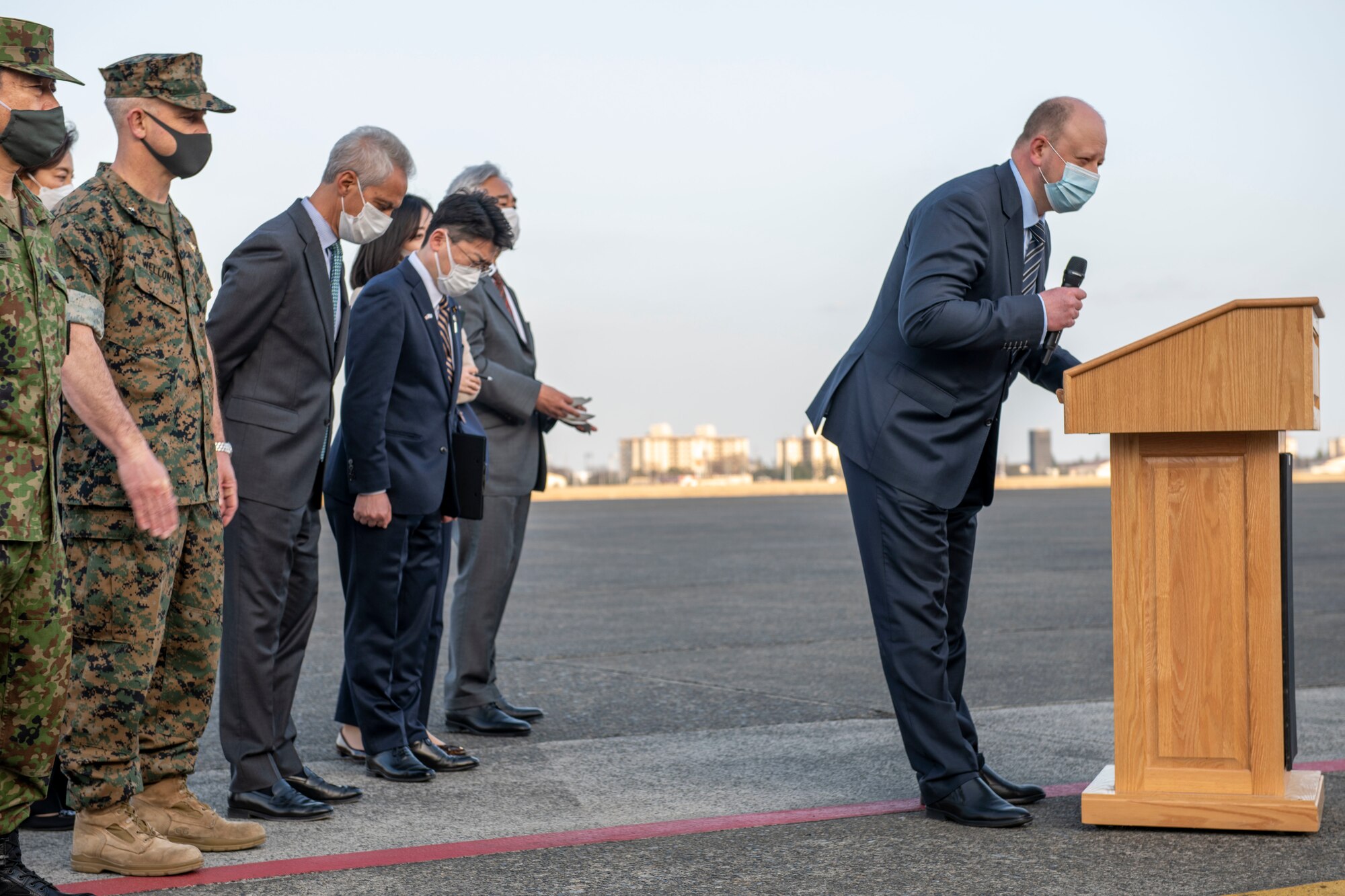 A line of political officials bow to a crowd of reporters.
