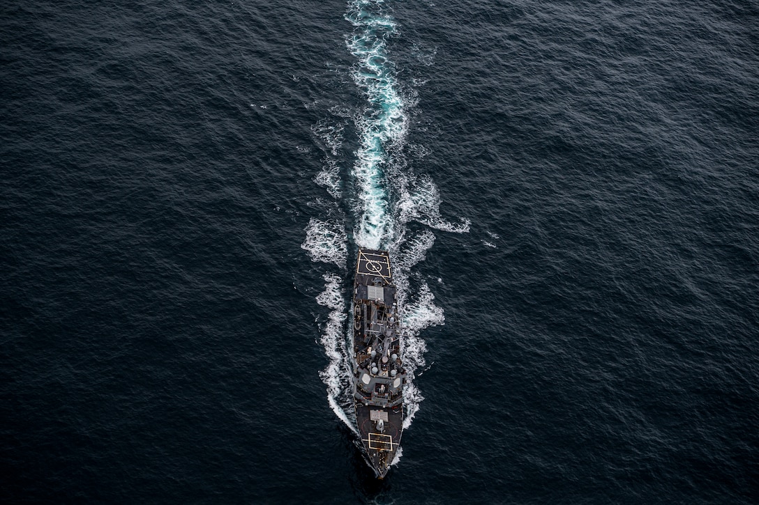 A military ship steams across dark blue water.