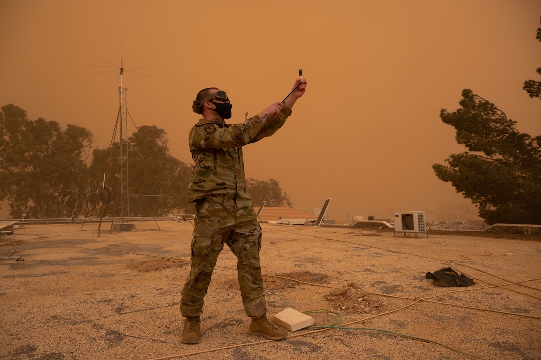 An airman uses a weather device during a dust storm.