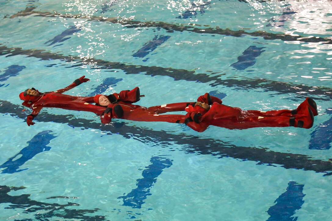 Three sailors form a line while floating on their backs in a pool.